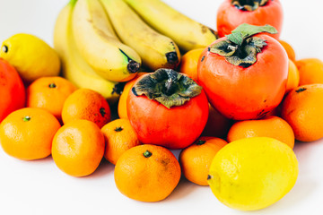 Fruit plate on white background. Mandarins, bananas, persimmons and lemons.