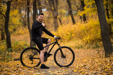 Fototapeta na wymiar Handsome man biker in professional sportswear looking to side while riding bike down park alley on autumn day. Sportsman training thinking about future win in contest
