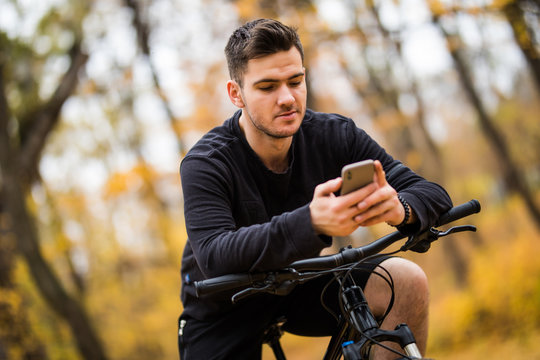 Young Sportsman Riding Bicycle Holding Phone, Sunny Autumn Park