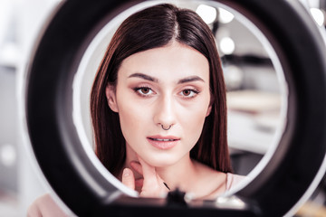 Serious nice woman looking at her face in the mirror