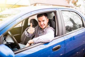 Happy smiling man sitting inside car showing thumbs up. Handsome guy excited about his new vehicle. Positive face expression