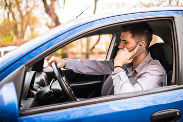 Portrait of young handsome man driving car and speaking on mobile phone.
