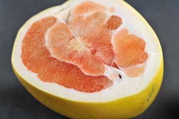 Half pink pomelo on a dark background. Fruit occupies the entire space of the frame. Close-up. Macro shooting.
