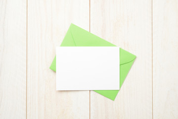 Sobre verde y tarjeta en blanco en la mesa de madera blanca