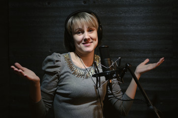 Confused woman a singer in a headphones is guiltily spreading hands in a sound recording studio room.