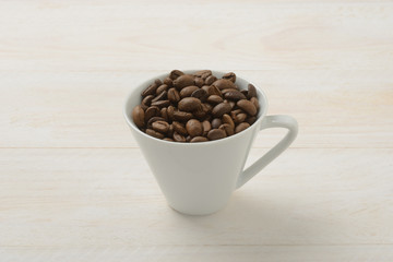 Granos de café en una taza en la mesa de madera blanca