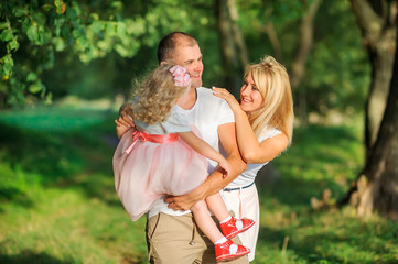 Fototapeta premium Happy family in a beautiful spring park, dad holds a daughter in his arms, having fun and smiling, healthy outdoor recreation