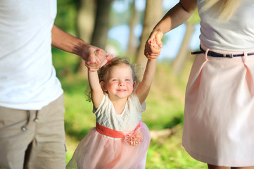 Fototapeta premium Happy family walks in a beautiful spring park, parents hold their daughter by the hands, healthy outdoor recreation