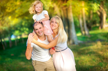 Naklejka premium Happy family in a beautiful spring park, daughter around dad's neck, healthy outdoor recreation