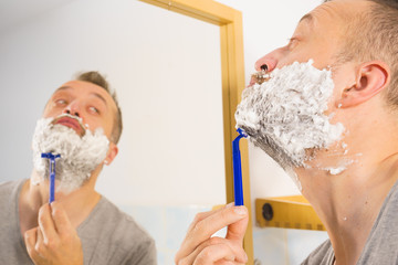 Guy shaving his beard in bathroom