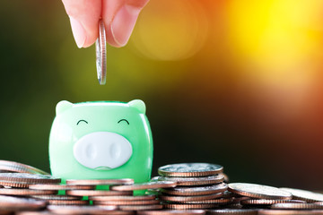Businessman hand hold a coin with save in the piggy bank put on the coin on sunlight in the public...