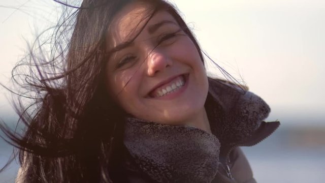 Happy cute young woman smiling looking camera with wind blowing her long hair in winter super slow motion