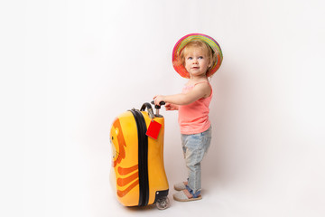Funny curly little baby girl in a hat, T-shirt and jeans with a yellow suitcase is smiling on a white background waiting for an airplane. concept trip with kids