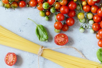 Food frame. Pasta ingredients concept. Uncooked spaghetti and cherry tomato with green basil on a blue background. Top view with copy space. Italian food