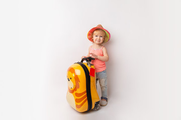 Funny curly little baby girl in a hat, T-shirt and jeans with a yellow suitcase is smiling on a white background waiting for an airplane. concept trip with kids