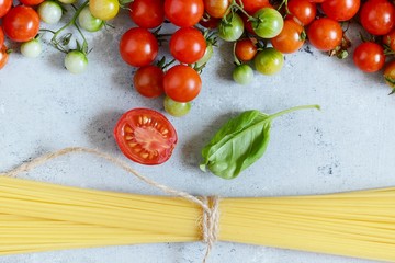 Food frame. Pasta ingredients concept. Uncooked spaghetti and cherry tomato with green basil on a blue background. Top view with copy space. Italian food
