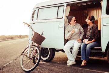Adult aged caucasian happy couple sit down out of a vintage van drinking a tea and enjoying the...