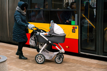Woman with baby carriage getting into a bus on the station. Woman with stroller in the city
