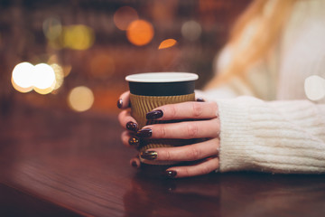 female hands holding a paper cup with hot coffee