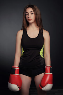 Young fitness girl with bloxing gloves looking at camera over black background
