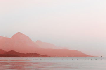 Coral sunset at the sea with mountains silhouettes in the fog. Beautiful evening seascape.
