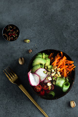 Vegan buddha bowl. Bowl with fresh raw vegetables - carrot, zucchini, tomatoes cherry and avocado, almonds. Dark grey background, top view