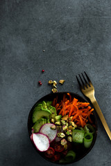 Vegan buddha bowl. Bowl with fresh raw vegetables - carrot, zucchini, tomatoes cherry and avocado, nuts. Dark grey background, top view, copy space