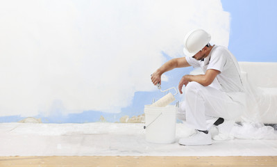painter man at work takes the color with paint roller from the bucket, blank white wall for copy...