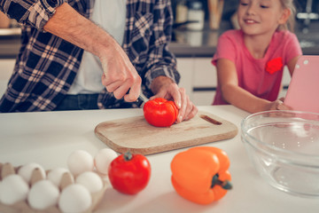 Tall bearded dark-haired man cutting a tomato for salad