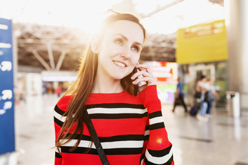 Positive young female with a suitcase in her hand talking on the phone with her husband agreeing on a meeting place after a long separation