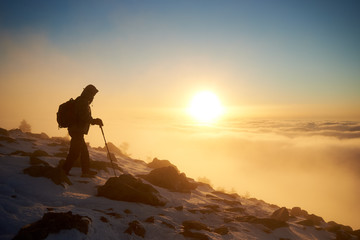Tourist climber with backpack and trekking poles on rocky snowy mountain steep slope on copy space...