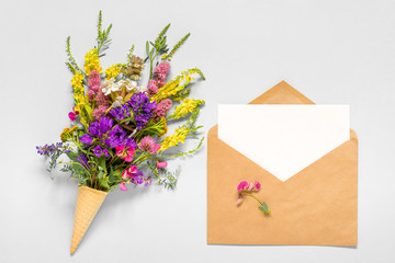 Bouquet field colored flowers in waffle ice cream cone and craft envelope with empty blank paper card for text on grey background Creative Flat Lay Top view Mock up Concept Women's day or Mothers Day