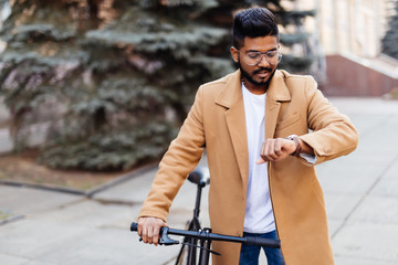Handsome young indian hipster enjoying a bike ride and checking time on his watch.