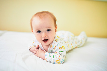 Baby girl in pyjamas having fun on bed in nursery