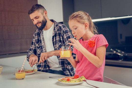 Bearded tall man in a checkered shirt and his cute daughter eating omelet