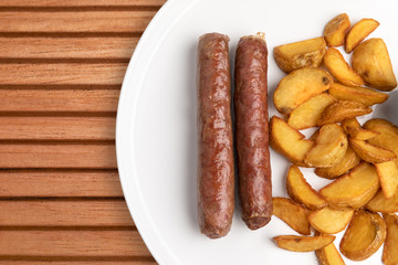 beef sausages and fried potatoes on white plate and table. wooden table made from slats. cafe menu