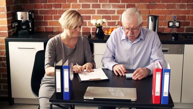 Mature, worried couple counting bills with smartphone in the kitchen
