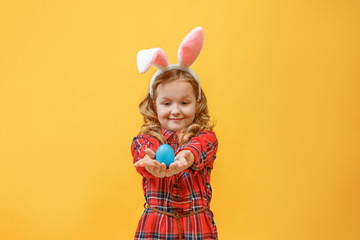 Obraz na płótnie Canvas Cheerful little kid girl with bunny ears with an easter egg on a colored background.