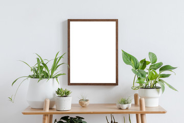 Scandinavian room interior with mock up photo frame on the brown bamboo shelf with beautiful plants in differents hipster and design pots. White walls. Modern and floral concept of shelfs.