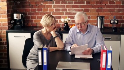 Mature, worried couple sitting with documents in the kitchen
- Powered by Adobe