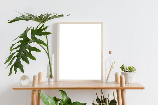 Scandinavian room interior with mock up photo frame on the brown bamboo shelf with beautiful plants, tropical leafs and accessories. White walls. Modern and floral concept of shelfs.