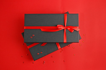 Black gift box with a red ribbon on a red paper background with two hearts love gift for...
