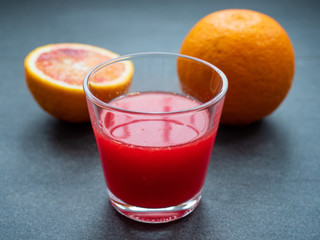 Glas mit Blutorangensaft und Orangen auf dunklem Untergrund