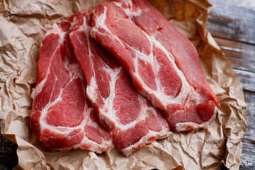Thinly sliced fresh raw red meat on craft cooking paper on wooden table.