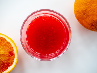 Glas mit Blutorangensaft und Orangen auf weißen Untergrund