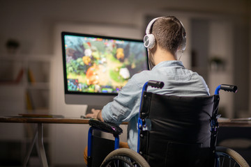 Rear view of editor or video designer in headphones sitting in wheelchair in front of computer screen and working with new content