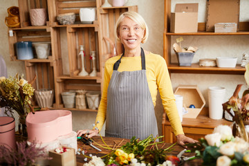 Waist up portrait of mature florist posing in flower shop and looking at camera, copy space