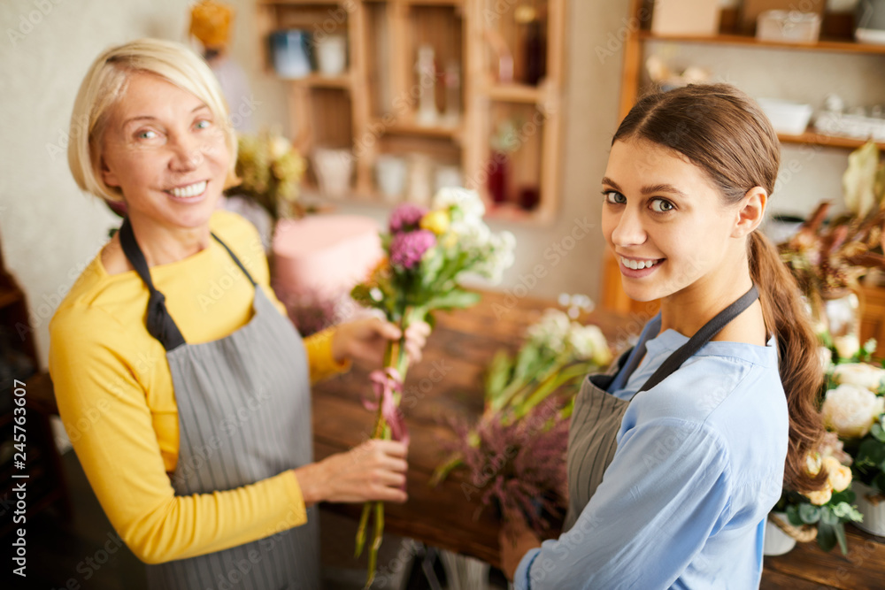 Wall mural high angle portrait of two female florists looking at camera and smiling while working in flower sho