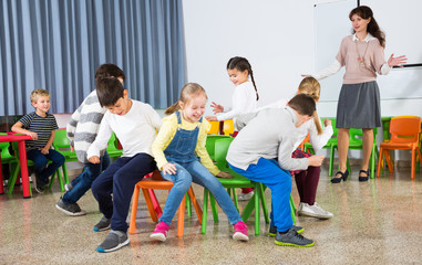 Pupils with teacher playing musical chairs - obrazy, fototapety, plakaty