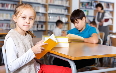 Fototapeta na wymiar Portrait of cute preteen girl preparing for lesson in school library, reading textbooks